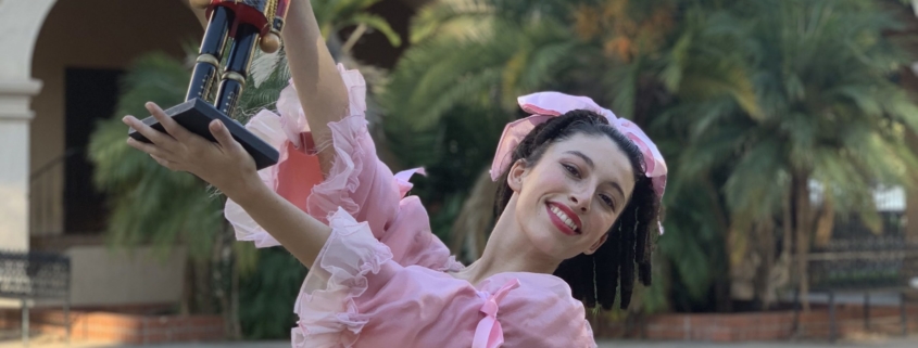 shot of a young ballerina playing Clara in a pink dress holding up a nutcracker