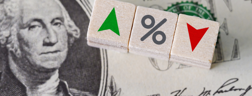 set of dice with a green arrow, percent sign and red arrow sitting on top of a dollar bill
