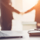 Business people shaking hands with a laptop and notebook in the foreground